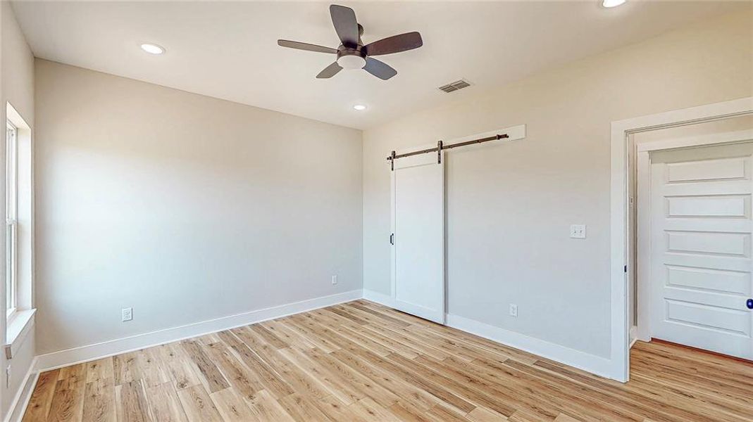 Unfurnished bedroom with a barn door, light wood-type flooring, recessed lighting, and a ceiling fan Unfurnished bedroom with a barn door, light wood-type flooring, recessed lighting, and a ceiling fan