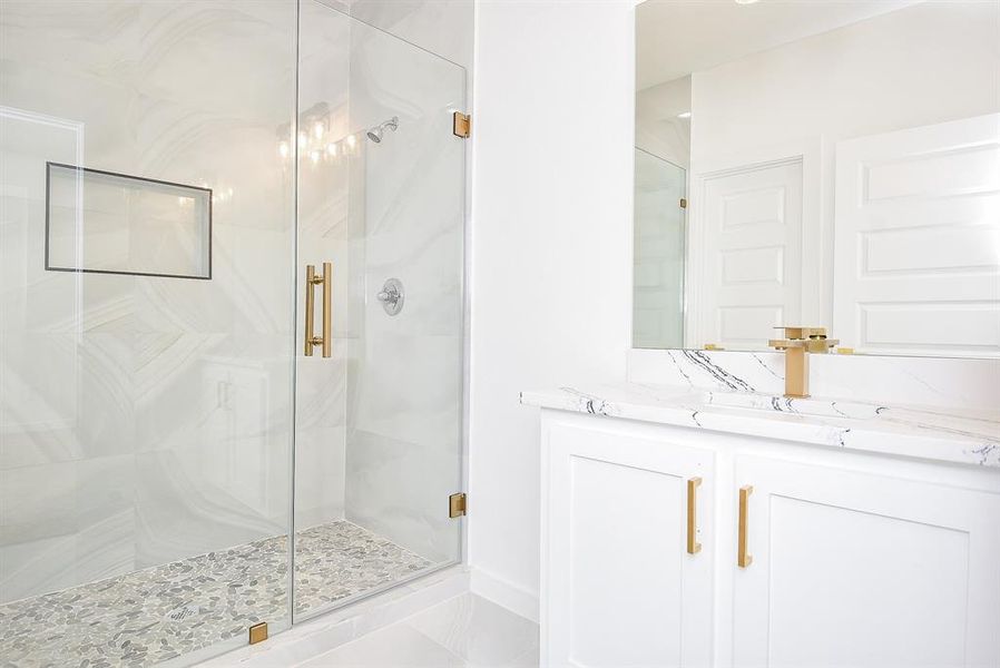 Elegant secondary full bathroom featuring a walk-in shower with polished porcelain tile walls, a sleek glass enclosure, and gold accents. The single vanity with a quartz countertop adds a touch of modern luxury.