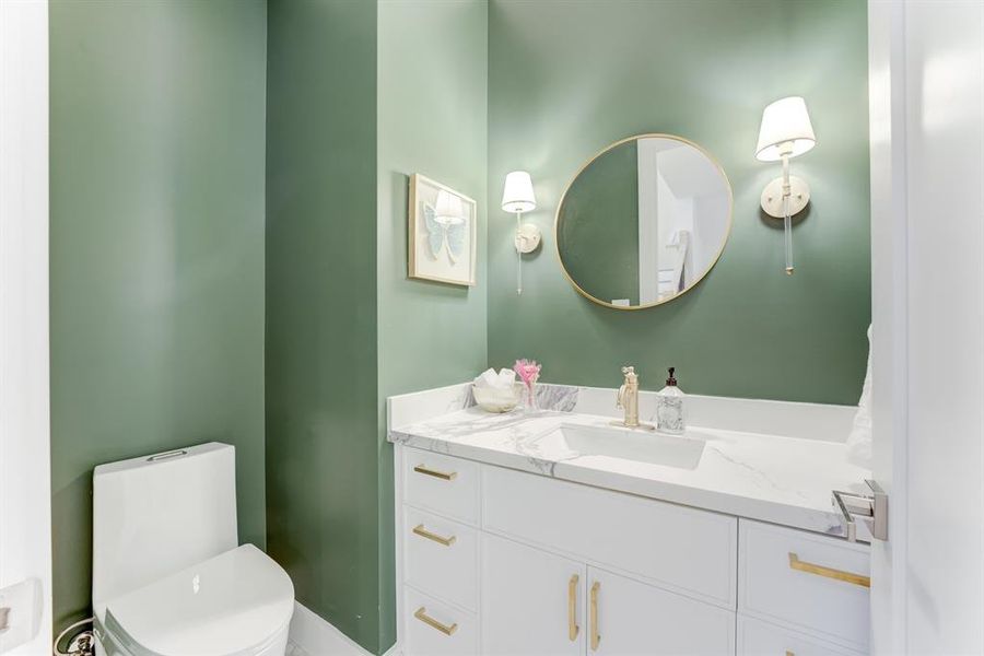 This gorgeous green half bathroom has custom pendant lighting, gold hardware, white cabinetry, quartz countertops, and chic patterned tile flooring.