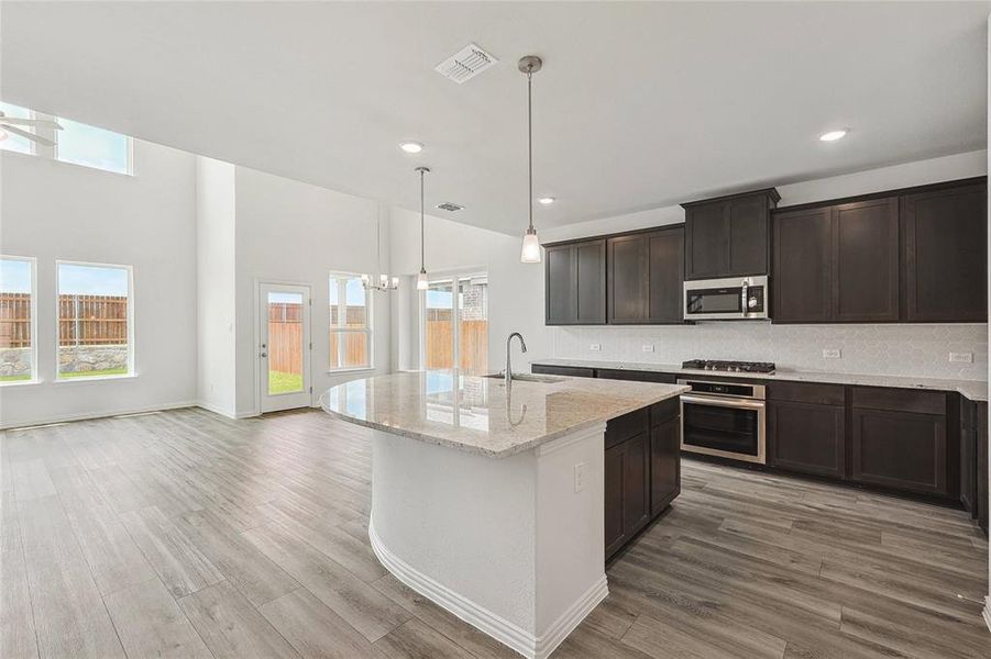 Kitchen featuring appliances with stainless steel finishes, tasteful backsplash, sink, light wood-type flooring, and light stone countertops