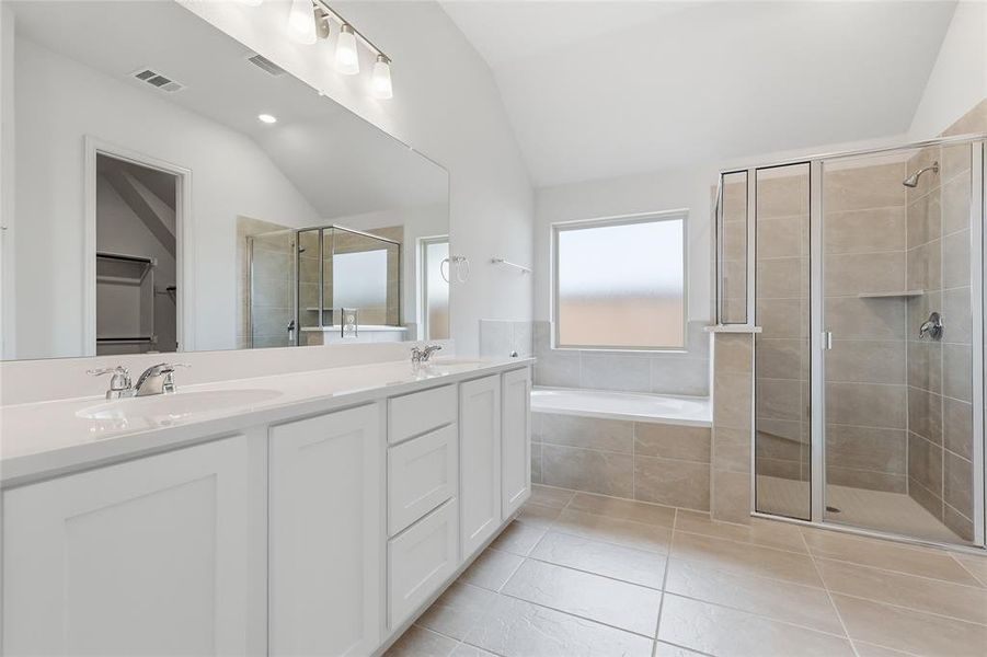 Full bathroom featuring double vanity, a stall shower, vaulted ceiling, a bath, and light tile patterned floors