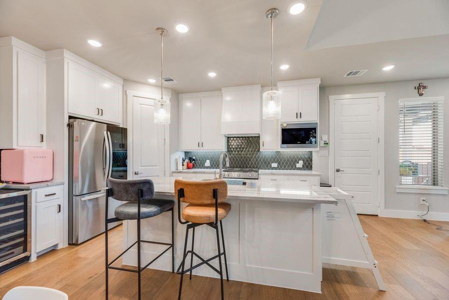 Kitchen with a kitchen island with sink, white cabinetry, and wine cooler
