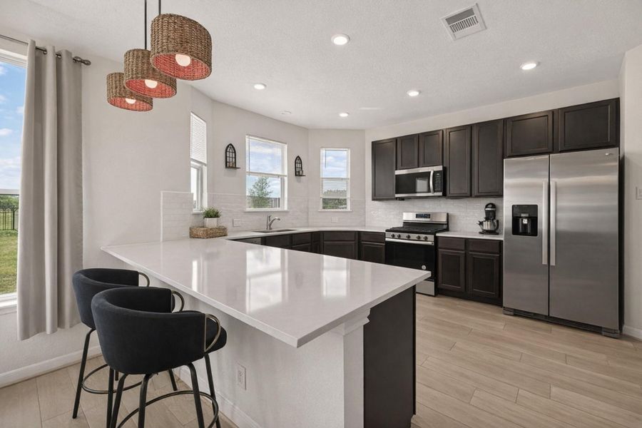 U-shaped kitchen shines with quartz counters, subway tile backsplash, recessed lighting, and abundant cabinetry.