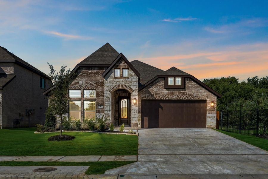 Single-story home with brick and stone exterior, arched entry, two-car garage, and manicured front lawn at dusk.