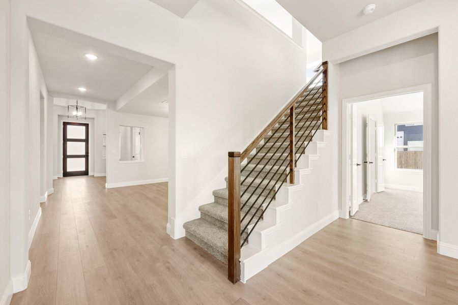 Bright home entryway with carpeted staircase, wood railing, light hardwood floors, and front door with pendant light