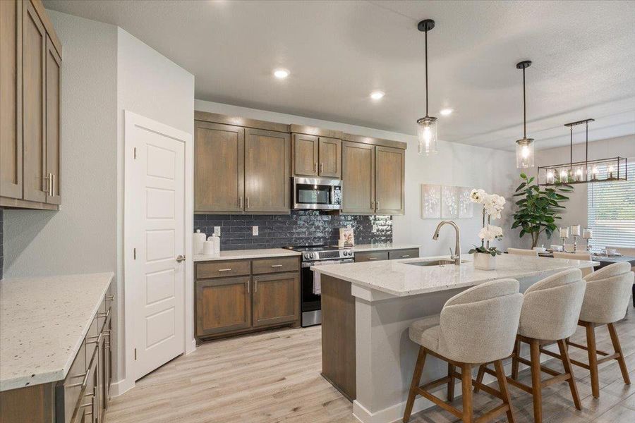 Kitchen featuring decorative light fixtures, light stone countertops, decorative backsplash, appliances with stainless steel finishes, and a breakfast bar area Kitchen featuring decorative light fixtures, light stone countertops, decorative backsplash, appliances with stainless steel finishes, and a breakfast bar area