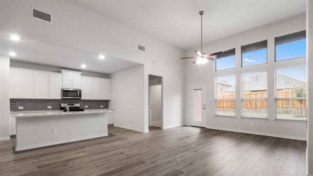 Kitchen with white cabinets, an island with sink, open floor plan, stainless steel appliances, and a ceiling fan