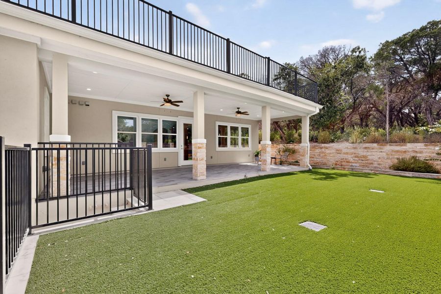 A covered patio opens onto a level grassy yard bordered by a stone retaining wall.