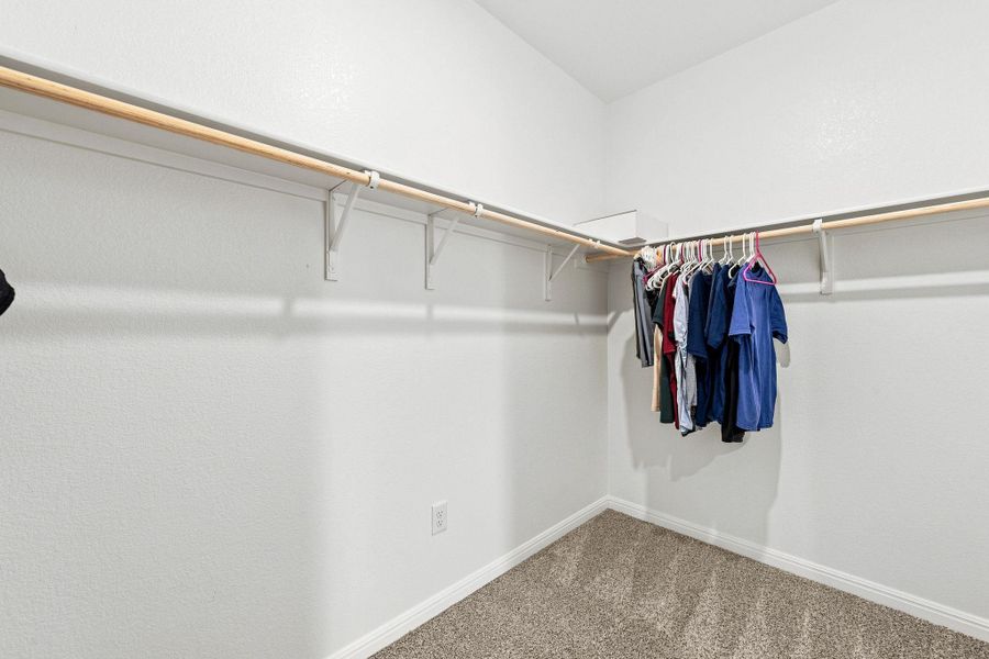 A spacious walk-in closet features plush carpeting and wrap-around clothing rods with overhead shelving.