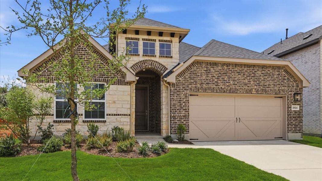 Brick and stone facade featuring an arched entryway, decorative garage door, dark shingle roof, and a landscaped front yard with mature shrubbery Brick and stone facade featuring an arched entryway, decorative garage door, dark shingle roof, and a landscaped front yard with mature shrubbery