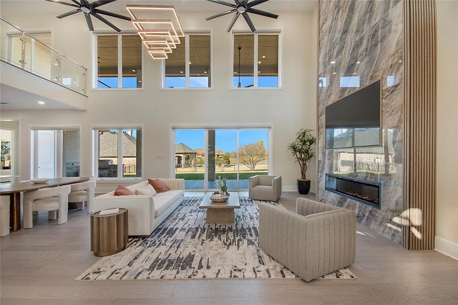 Living room featuring wood finished floors, a premium fireplace, ceiling fan, and a high ceiling Living room featuring wood finished floors, a premium fireplace, ceiling fan, and a high ceiling