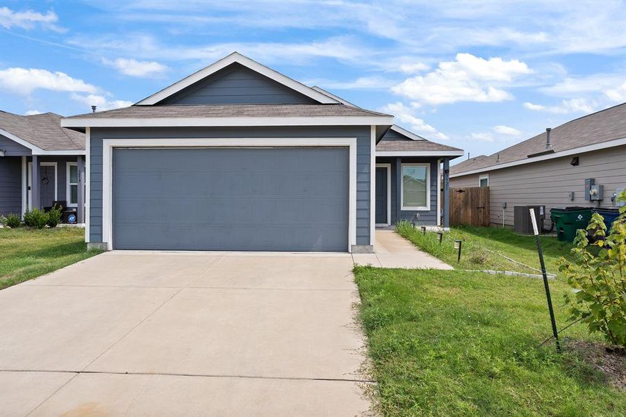 Ranch-style house with a front yard, driveway, roof with shingles, and a garage