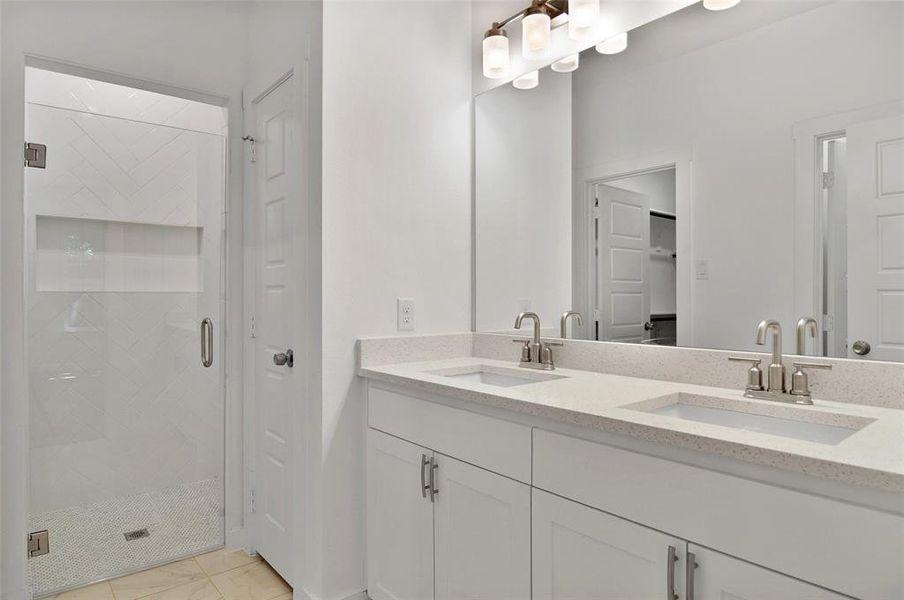 Bathroom featuring a shower with shower door, tile patterned flooring, and dual bowl vanity