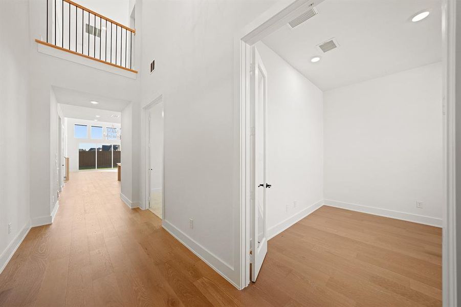 Corridor with recessed lighting, light wood-type flooring, and a high ceiling Corridor with recessed lighting, light wood-type flooring, and a high ceiling
