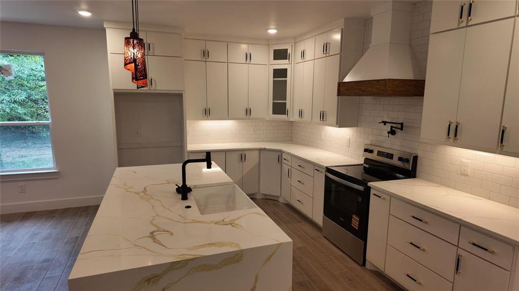 Kitchen with stainless steel electric range, wall chimney range hood, light stone countertops, backsplash, and white cabinets Kitchen with stainless steel electric range, wall chimney range hood, light stone countertops, backsplash, and white cabinets
