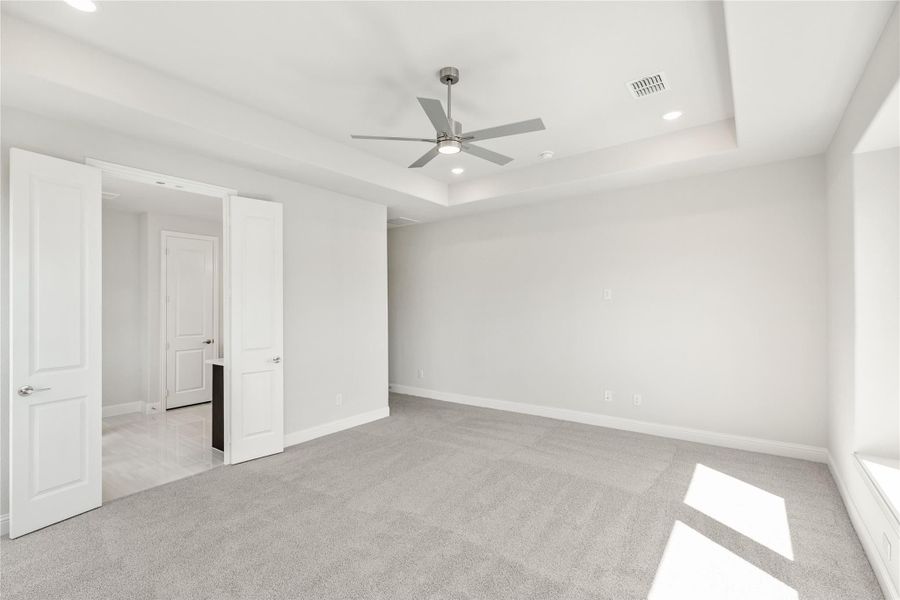 Empty bedroom with tray ceiling, ceiling fan, gray carpet, and white double doors Empty bedroom with tray ceiling, ceiling fan, gray carpet, and white double doors