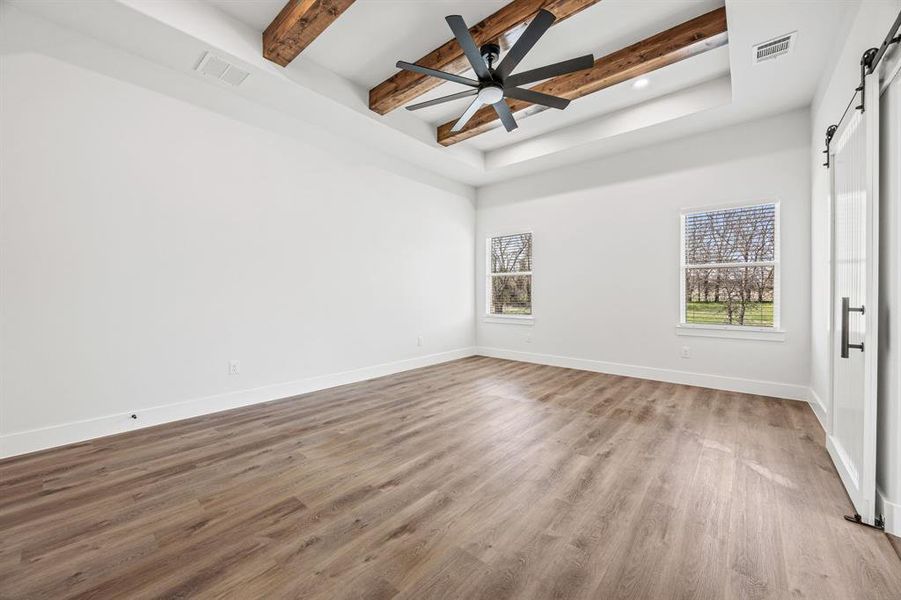 Empty room featuring a barn door, beam ceiling, a tray ceiling, wood finished floors, and recessed lighting Empty room featuring a barn door, beam ceiling, a tray ceiling, wood finished floors, and recessed lighting