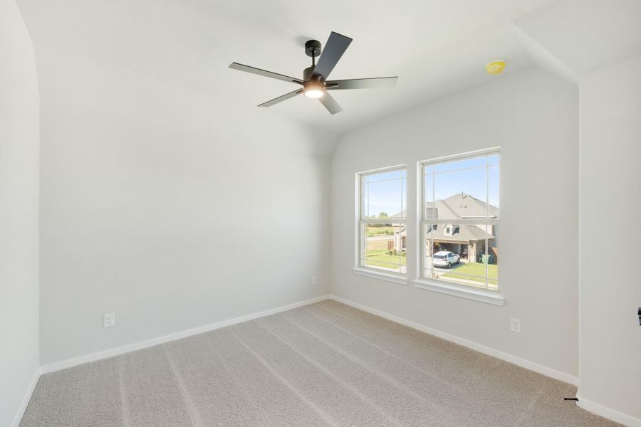 Empty bedroom with vaulted ceiling, ceiling fan, carpet flooring, and two windows overlooking neighborhood Empty bedroom with vaulted ceiling, ceiling fan, carpet flooring, and two windows overlooking neighborhood