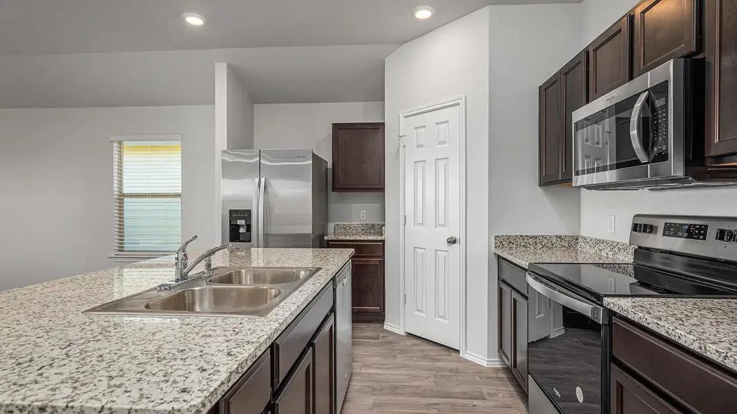 Kitchen featuring stainless steel appliances, dark wood finish cabinets, light wood-type flooring, a center island with sink, and recessed lighting Kitchen featuring stainless steel appliances, dark wood finish cabinets, light wood-type flooring, a center island with sink, and recessed lighting