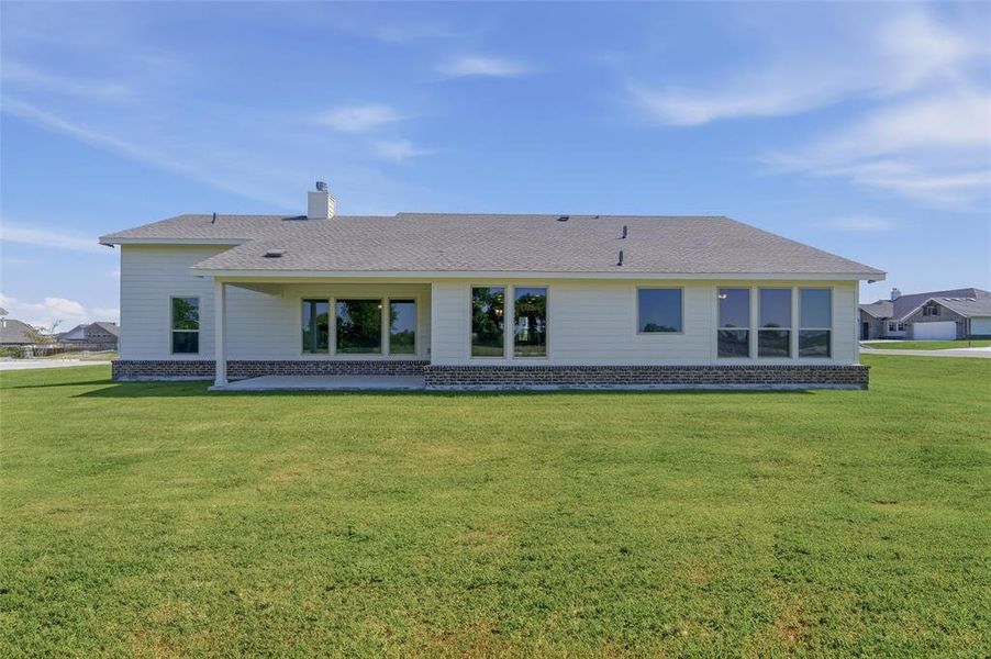 Rear exterior featuring a covered patio, extensive lawn, multi-pane windows, and stone detailing along the base