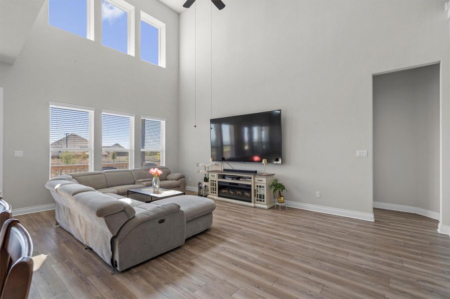 Double-height walls and handsome wood-look flooring frame a welcoming, light-filled living room.