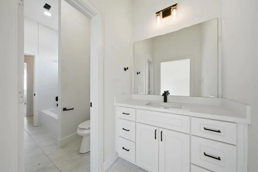 This jack and jill secondary bathroom features a sleek, modern design with a large vanity, ample storage, and a wide mirror.