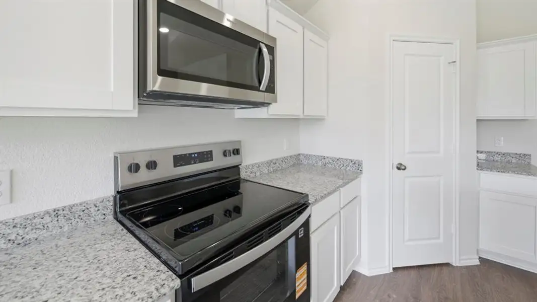 Kitchen with appliances with stainless steel finishes, light stone counters, white cabinets, and dark wood-style floors