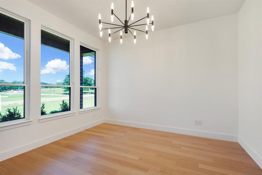 Spacious room featuring three large windows, a contemporary chandelier, light wood-finish flooring, and crisp white baseboards Spacious room featuring three large windows, a contemporary chandelier, light wood-finish flooring, and crisp white baseboards