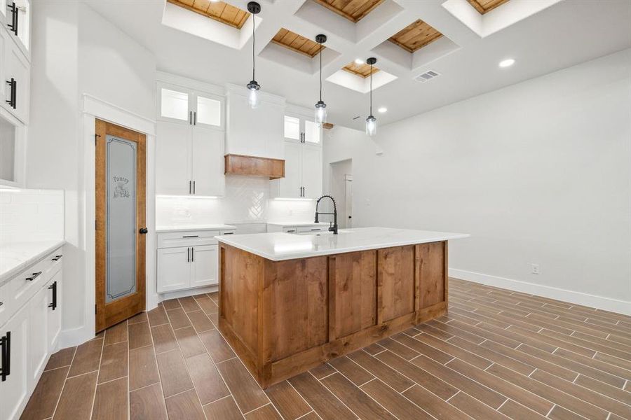 Kitchen featuring sink, white cabinetry, a skylight, pendant lighting, and a kitchen island with sink