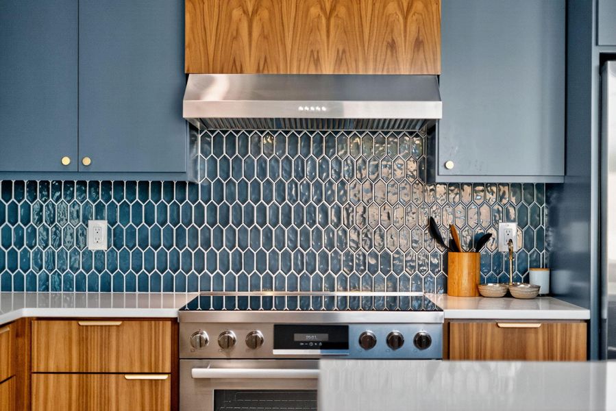 Kitchen with backsplash, stainless steel stove, ventilation hood, and light stone counters