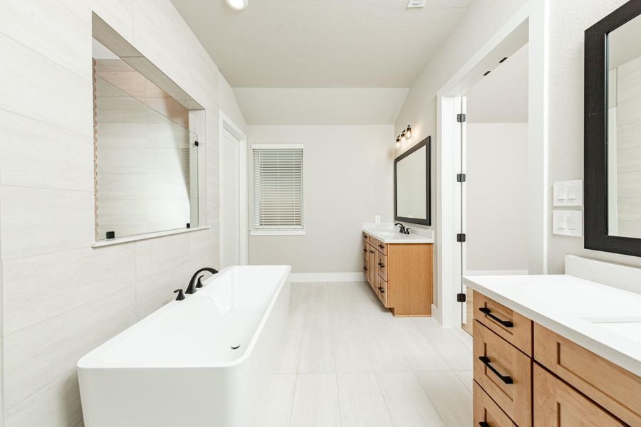 Modern primary bath features dual vanities with sleek white cabinetry, a quartz countertop, framed vanity mirrors, and black matte fixtures for a truly contemporary feel.