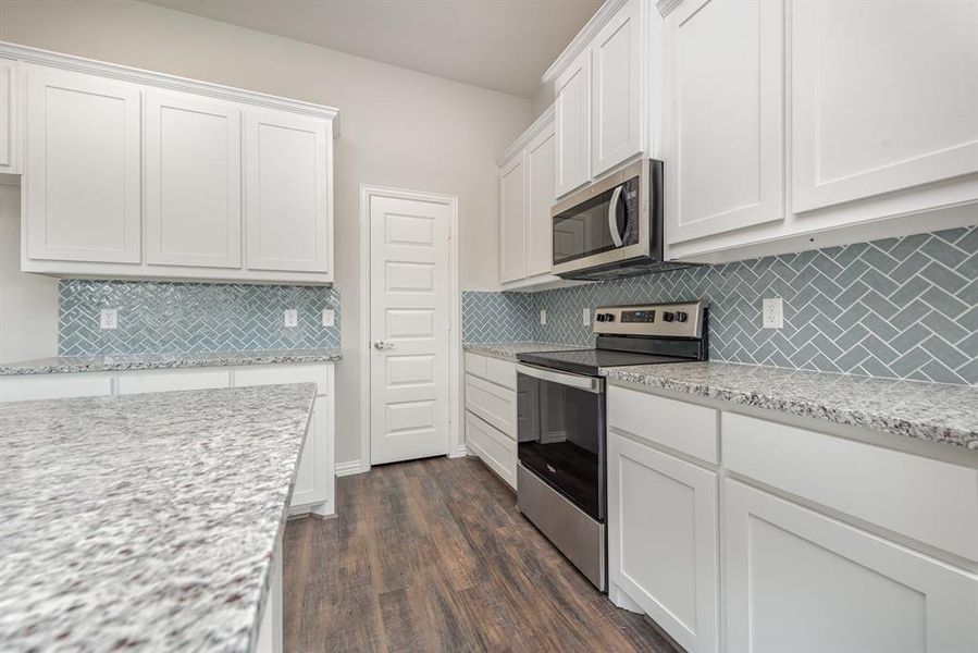 Kitchen with decorative backsplash, light stone countertops, stainless steel appliances, white cabinets, and dark hardwood / wood-style floors