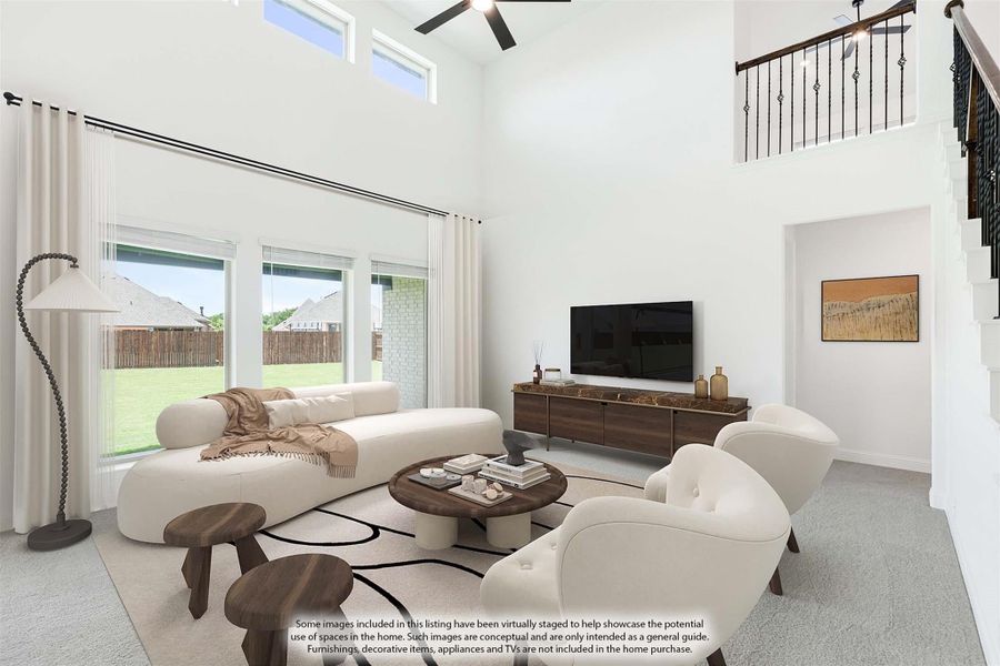 Living room with two-story ceiling, ceiling fan, large windows, and staircase with iron railing
