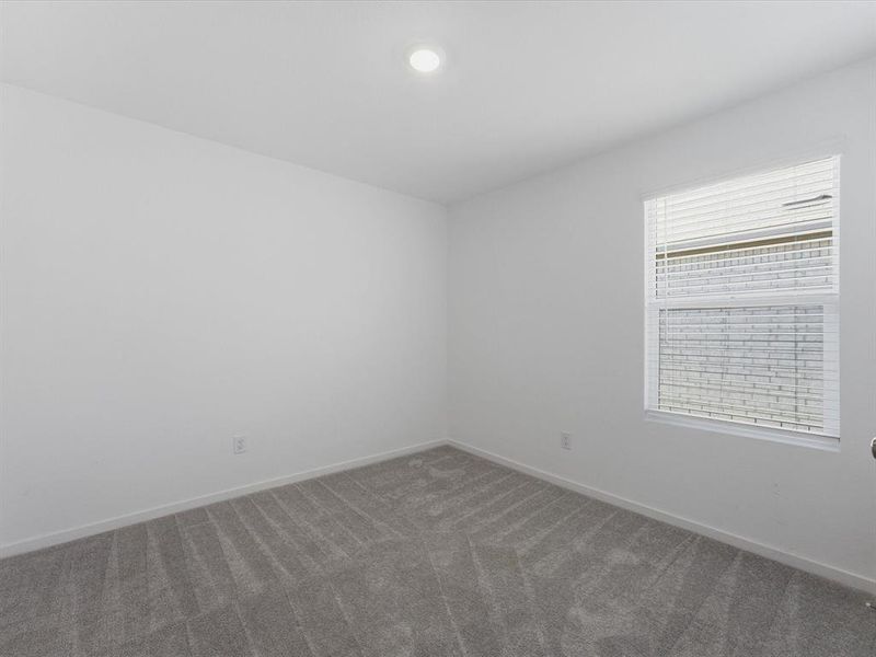 Bright room featuring a single window with horizontal blinds, overhead lighting, light gray walls, and gray patterned carpeting