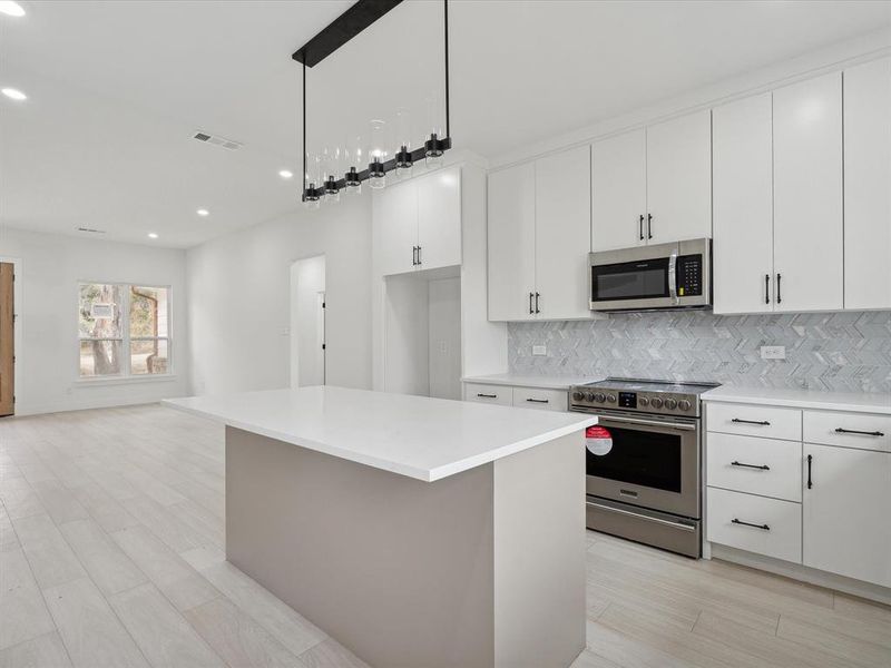 Kitchen with appliances with stainless steel finishes, light wood-type flooring, white cabinetry, and a kitchen island