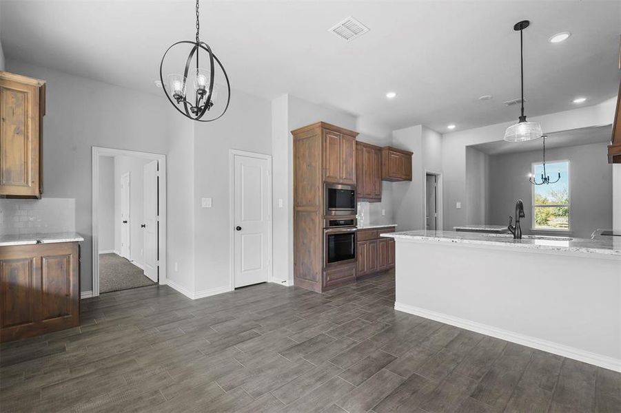 Kitchen featuring pendant lighting, light stone counters, appliances with stainless steel finishes, and dark hardwood / wood-style flooring