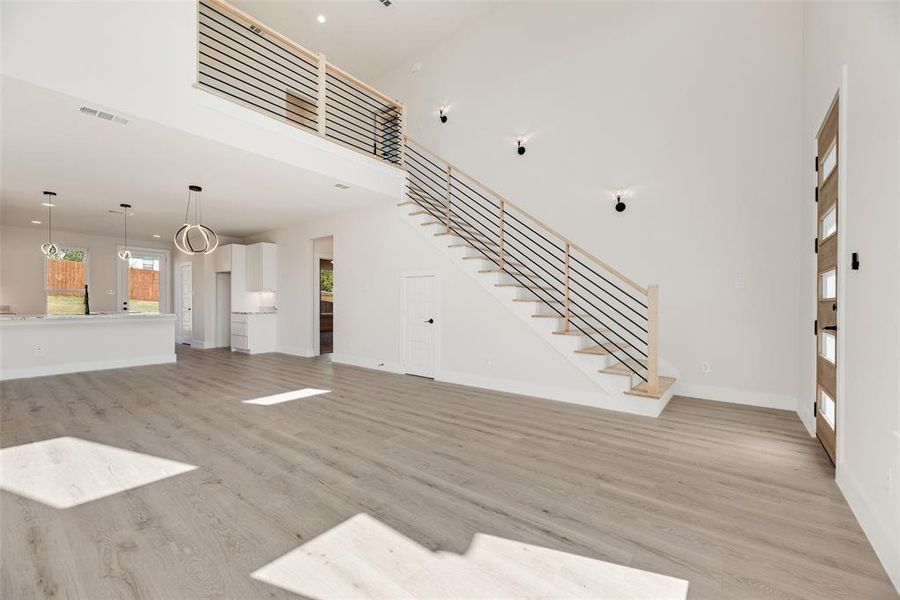Unfurnished living room featuring stairway, a towering ceiling, and light wood finished floors Unfurnished living room featuring stairway, a towering ceiling, and light wood finished floors