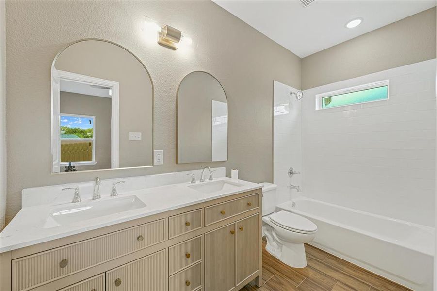 Full bath with shower / bathtub combination, healthy amount of natural light, double vanity, wood tiled floors, and a textured wall Full bath with shower / bathtub combination, healthy amount of natural light, double vanity, wood tiled floors, and a textured wall