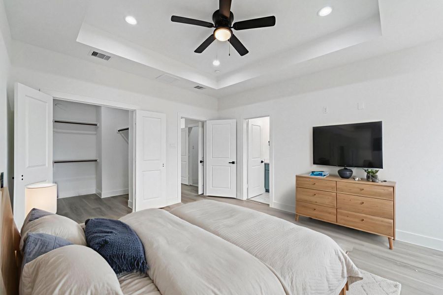 This Primary Bedroom features a tray ceiling with recessed lighting. The room includes a wide opening to a walk-in closet and has access to the primary bathroom.