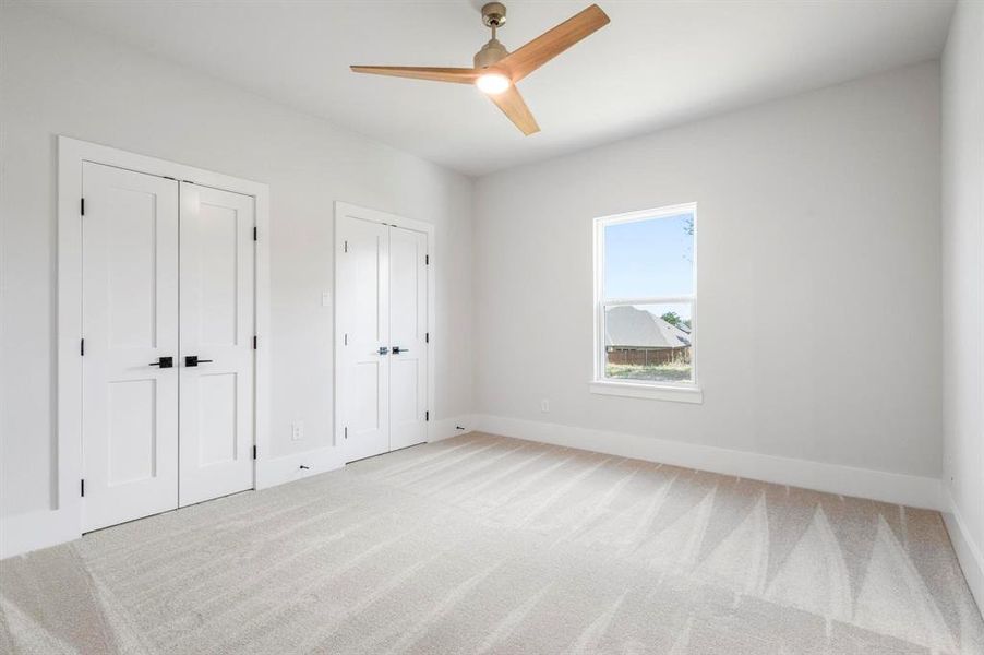 Unfurnished bedroom featuring carpet, two closets, and ceiling fan