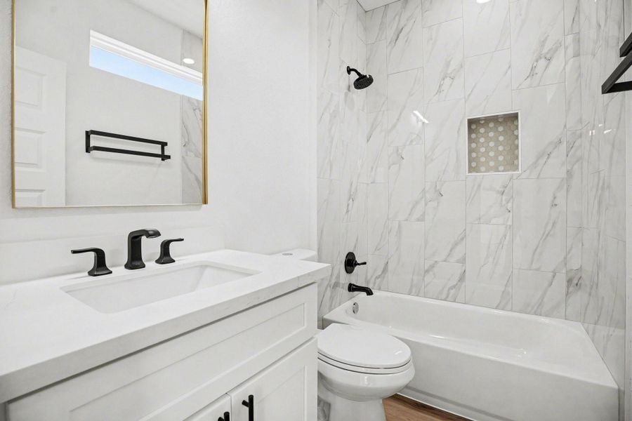 This modern bathroom features sleek white marble tile, a bathtub with a shower, and contemporary black fixtures. The vanity includes a large mirror and ample storage, creating a clean and elegant space.