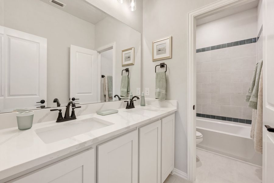 Bathroom with double sink vanity, white cabinets, and tiled shower-tub combo with dark fixtures