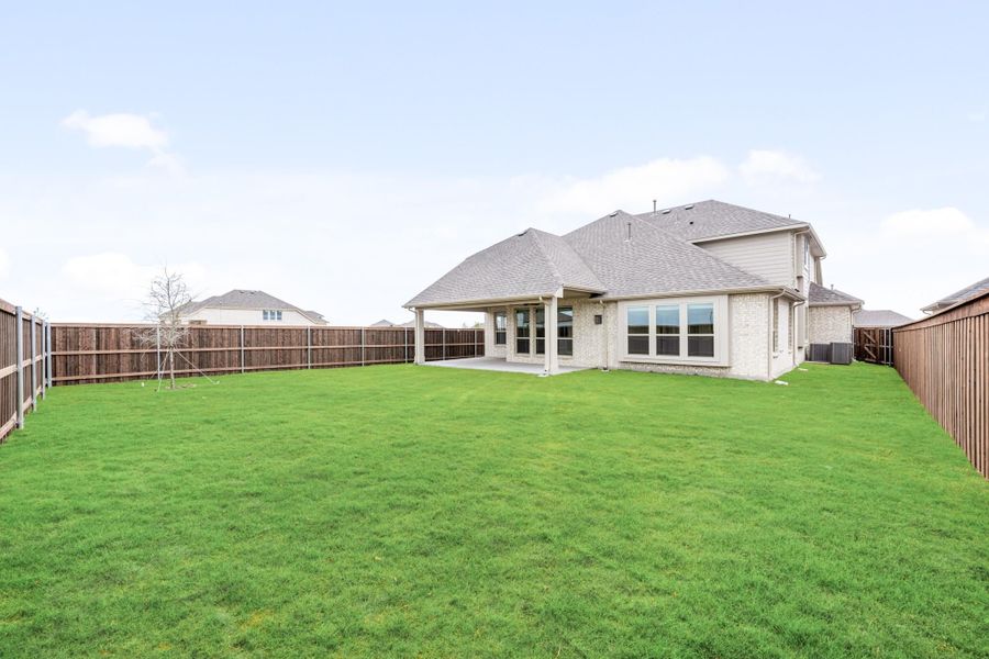 Backyard of two-story brick home with large green lawn, covered patio, and wood privacy fence