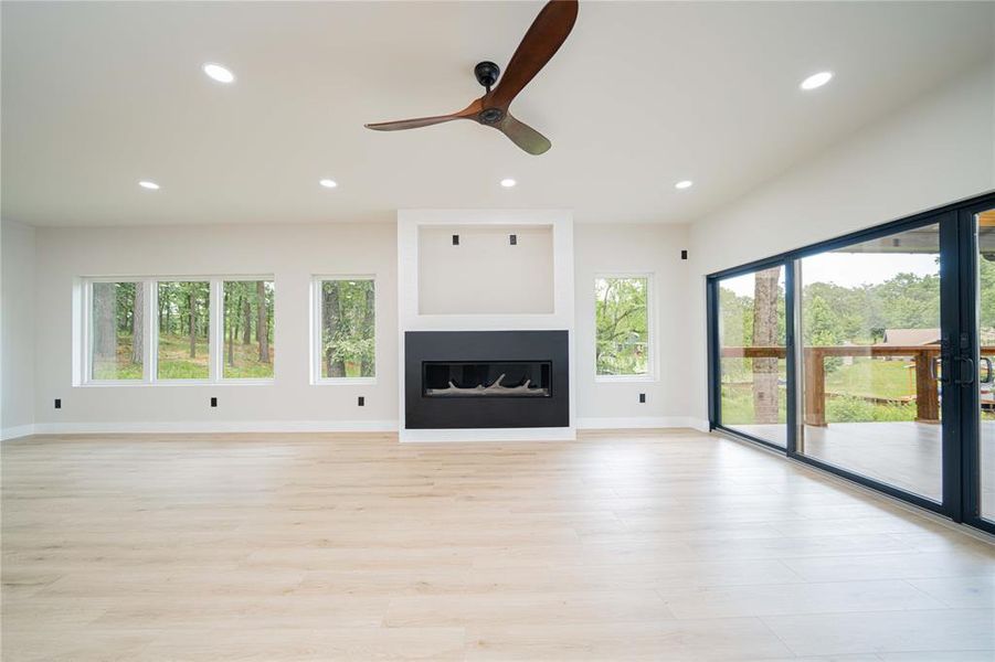 Unfurnished living room featuring plenty of natural light, recessed lighting, a ceiling fan, light wood finished floors, and a glass covered fireplace Unfurnished living room featuring plenty of natural light, recessed lighting, a ceiling fan, light wood finished floors, and a glass covered fireplace