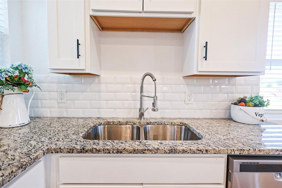 Kitchen with dishwasher, white cabinets, decorative backsplash, and light stone countertops
