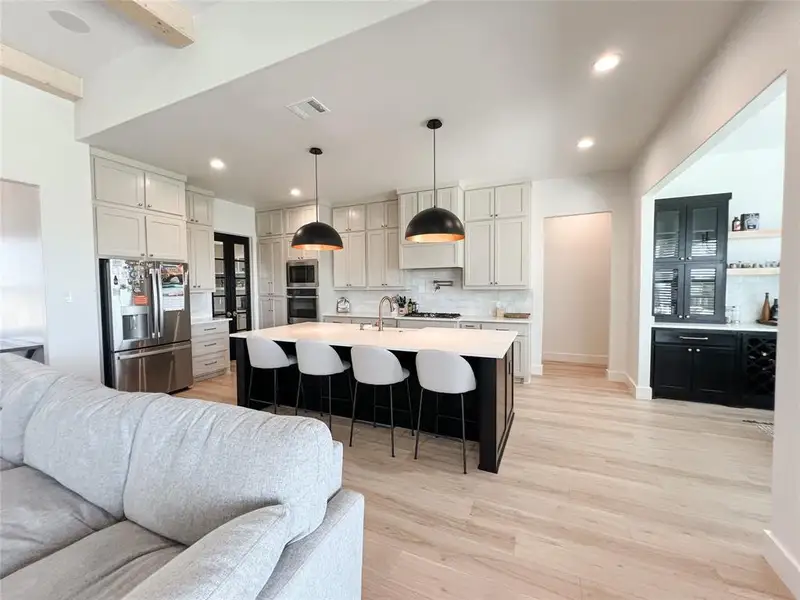 Kitchen with dark cabinetry, open floor plan, backsplash, appliances with stainless steel finishes, and hanging light fixtures