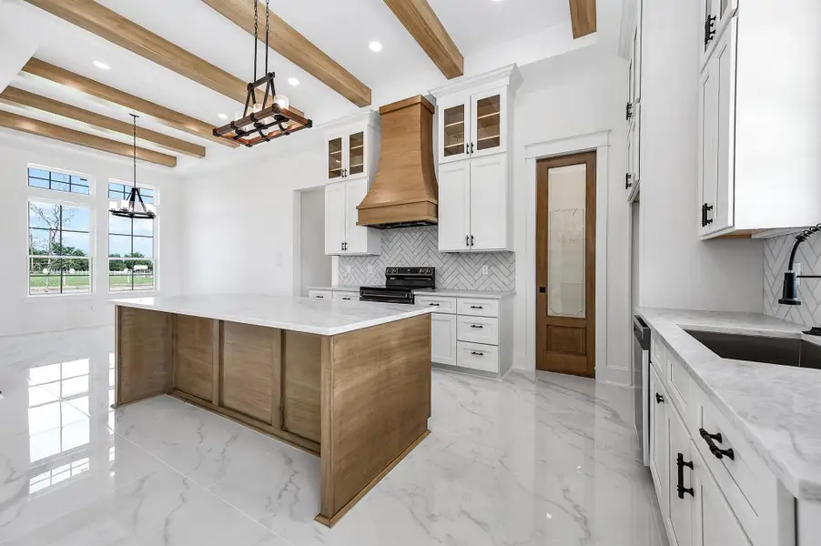Spacious kitchen with warm wood accents, custom cabinetry, a large island, and beautiful finishes, with windows bringing in plenty of natural light. Spacious kitchen with warm wood accents, custom cabinetry, a large island, and beautiful finishes, with windows bringing in plenty of natural light.