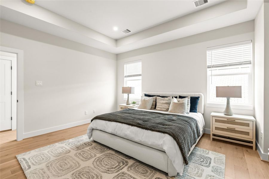 Natural light, warm engineered hardwood flooring, and a tray ceiling give the primary bedroom a bright, spacious feel.
