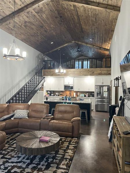 Barndominium living area featuring a chandelier, finished concrete flooring, stairs, high vaulted ceiling, and wooden ceiling Barndominium living area featuring a chandelier, finished concrete flooring, stairs, high vaulted ceiling, and wooden ceiling