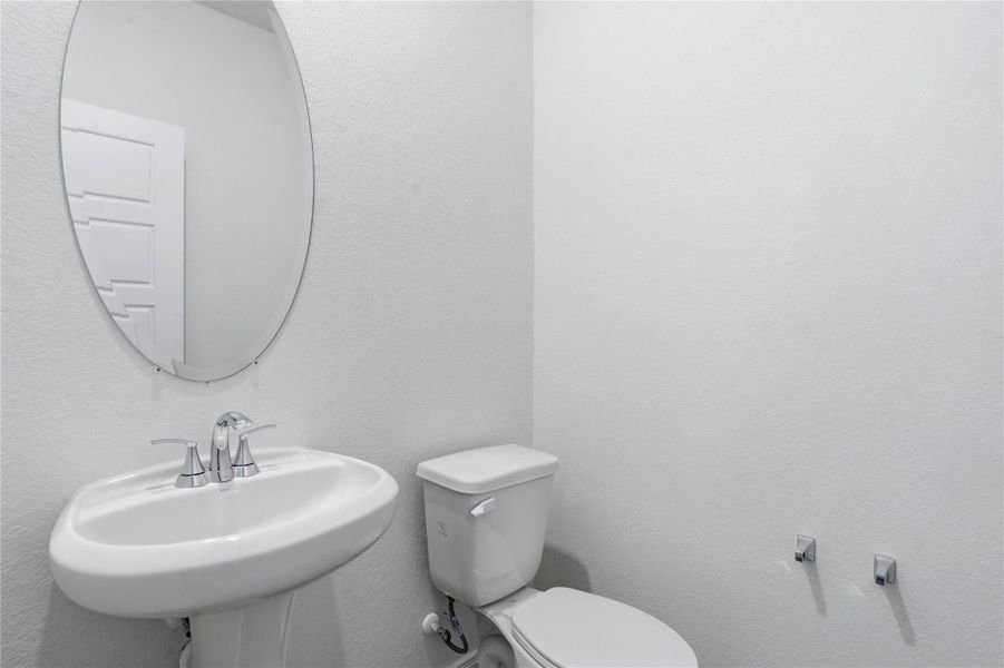 The powder room on the first floor includes a pedestal sink, oval mirror, and toilet to conveniently meet your needs.